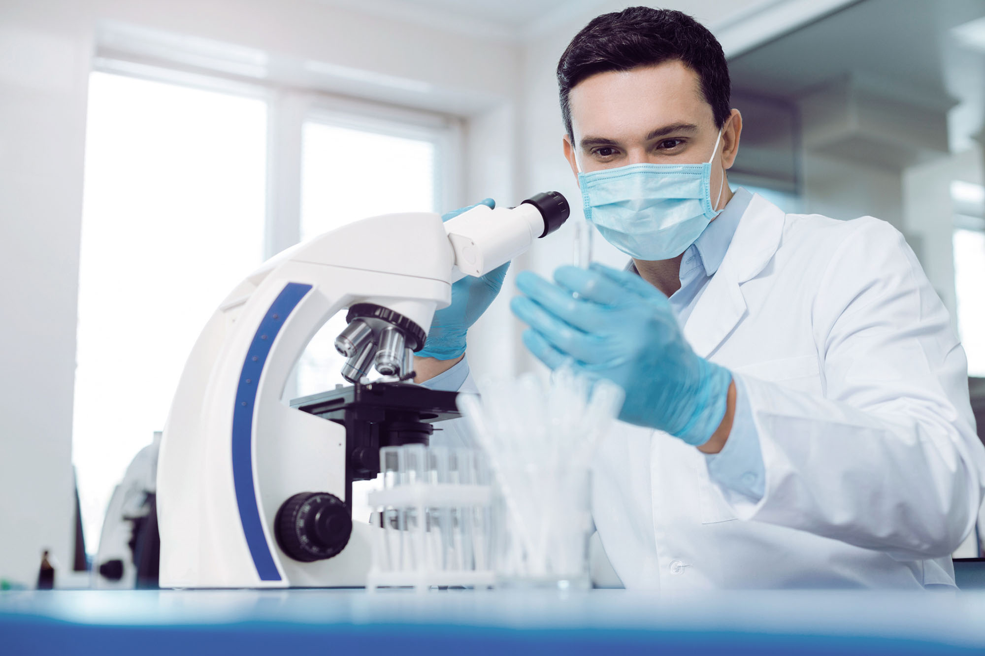 Young biologist sitting near the microscope and doing the research while working in the biological lab