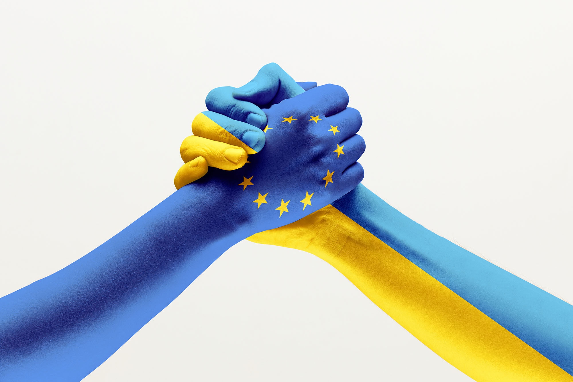 Two male hands holding colored in flag of European Unity and Ukraine isolated on grey studio background.