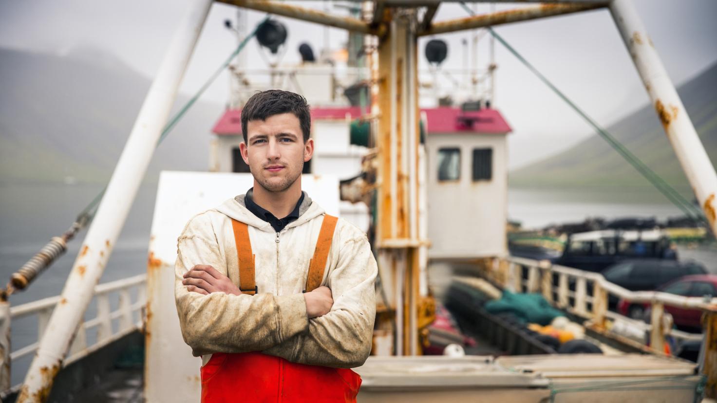 Ein Mann in Fischerausrüstung steht auf seinem Trawler