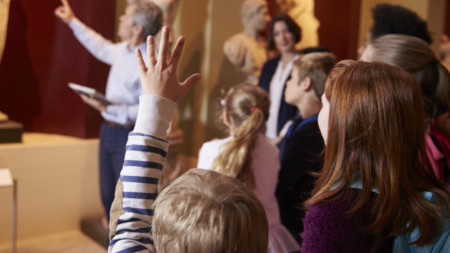 Младо момче, стоящо със съучениците си, вдига ръка