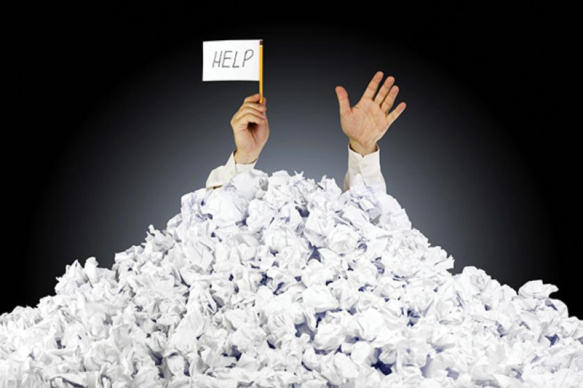 Person under crumpled pile of papers with help sign