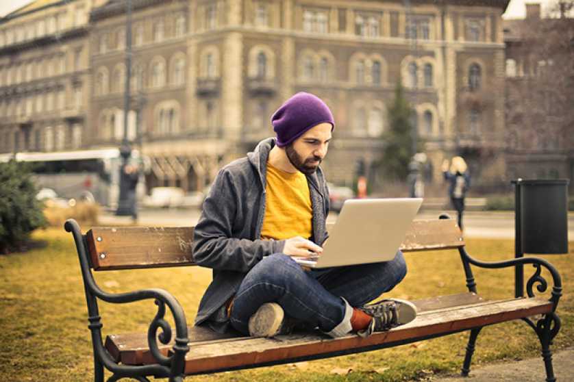 A young man sitting on a bench and working on a laptop