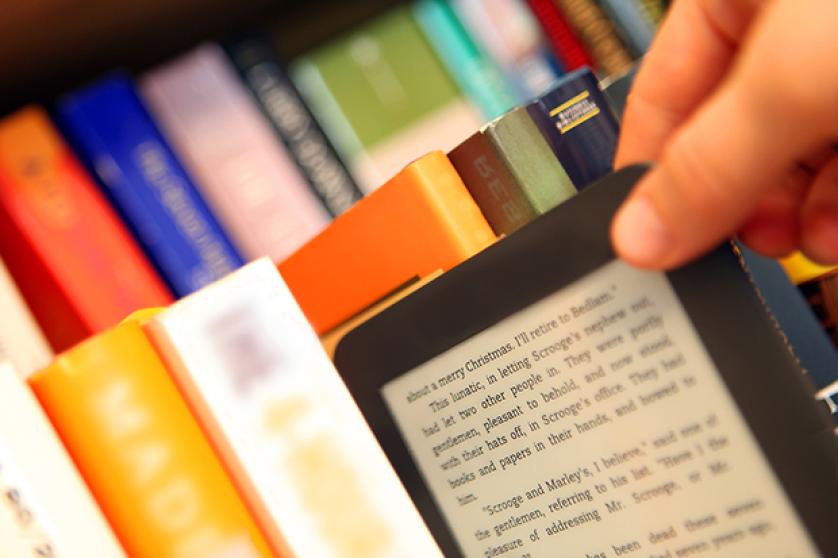 Hand Choosing an E-Book vs. Paper Books from a Bookshelf