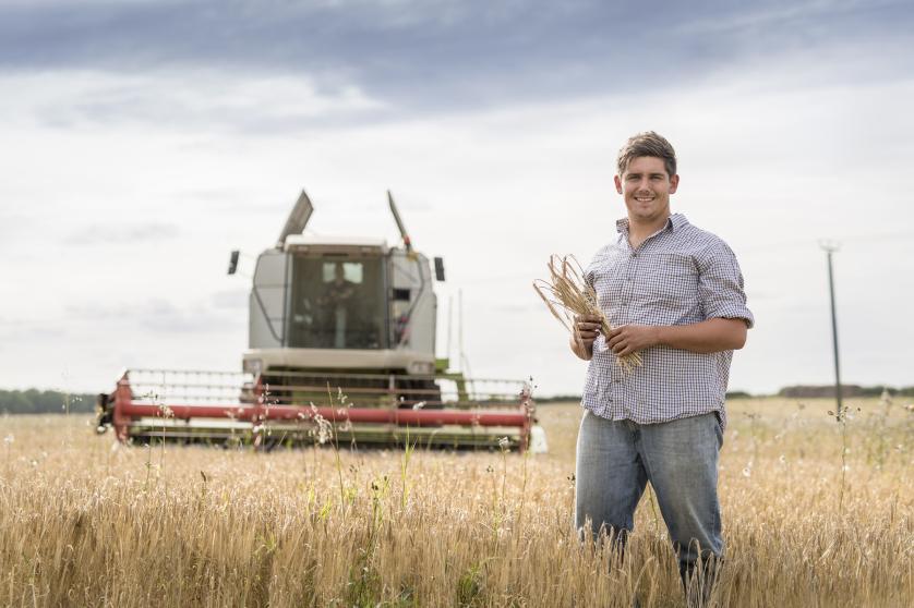 Muž na pšeničném poli stojí před traktorem.