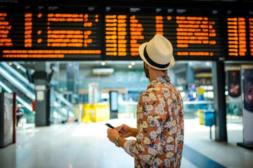 Ein Mann mit Hut schaut auf eine Abflugtafel in einem Bahnhof