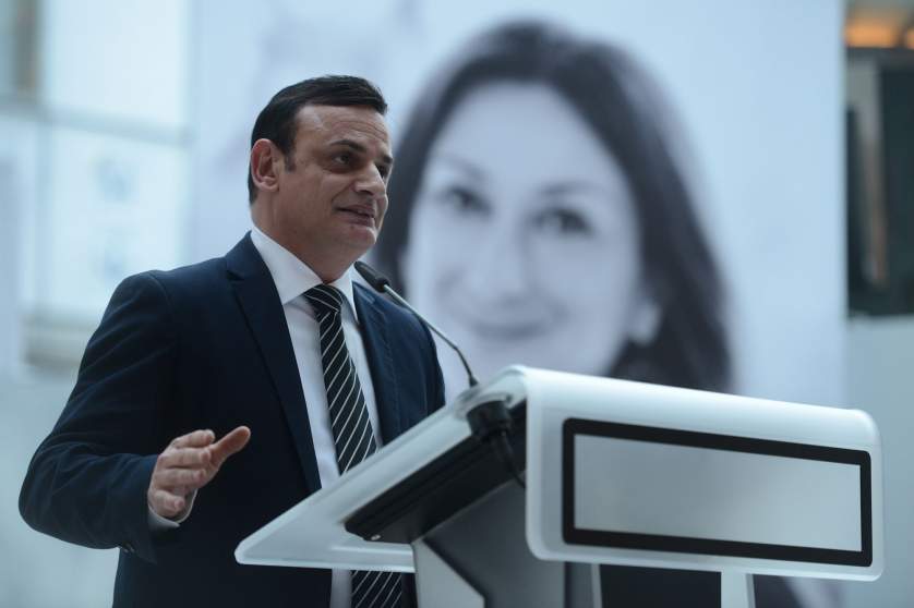 MEP David Casa giving a speech in Parliament with a portrait of slain journalist Daphne Caruana Galizia in the background.
