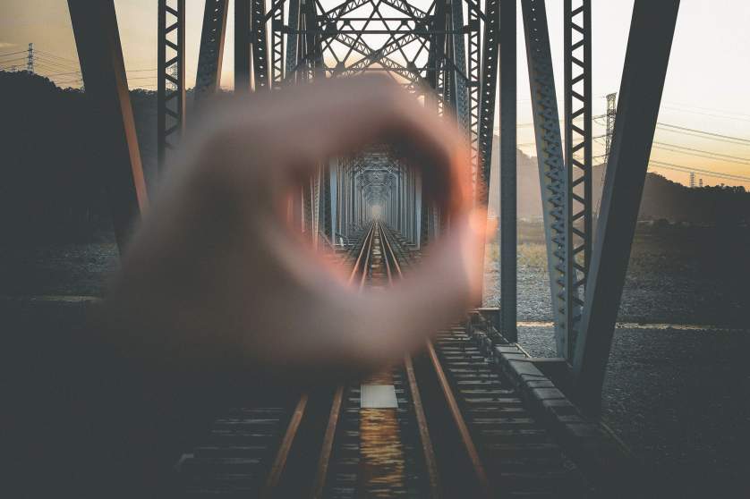 Cropped Hand Forming Circle In Front Of Railway Bridge