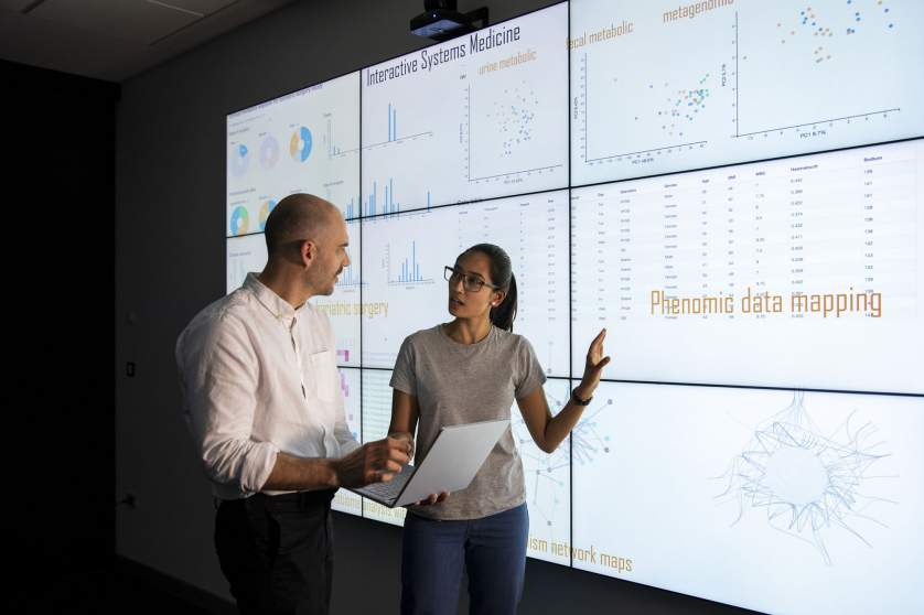 A lady showing her colleague a big screen of data. 