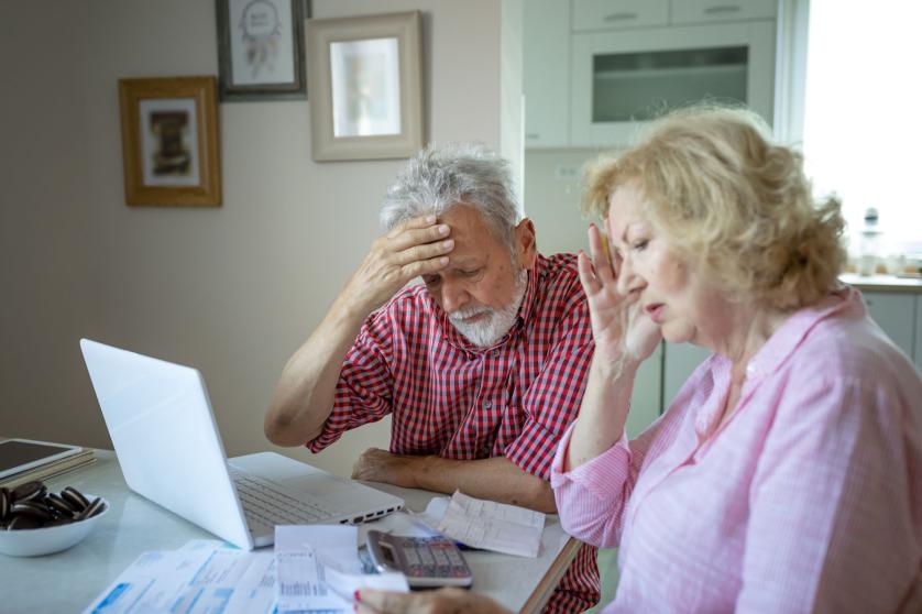 Elderly spouses sitting on couch at home planning budget check bills cheques