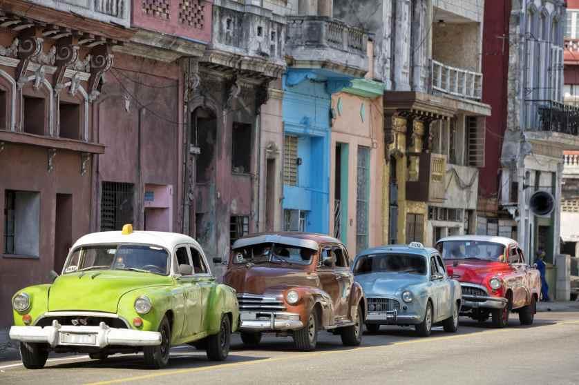 Vintage American cars speeding in front of dilapidated buildings in traditional colonial style