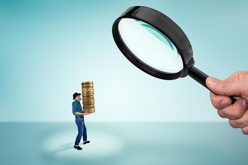 Man holding a stack of coins and big magnifying glass in hand