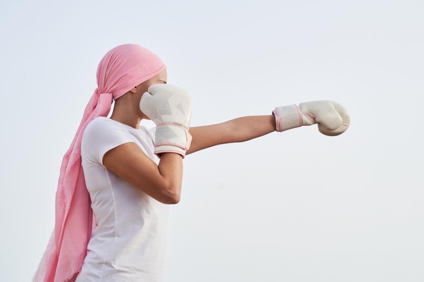Tunnistamaton naispuolinen syöpäpotilas, jolla on vaaleanpunainen huivi, nyrkkeilyasennossa nyrkkeilyhanskat käsissään taistelun merkiksi. Käsite syövän torjumisesta ja voittamisesta.