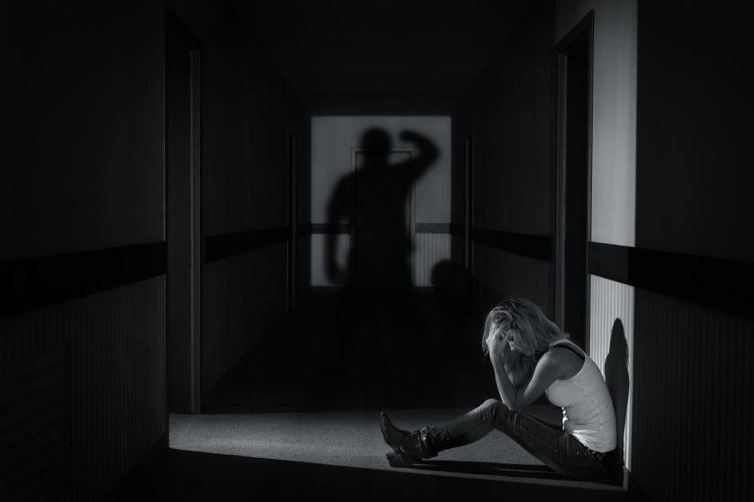 Fiatal nő ül egy üres folyosón, szemét eltakarva egy férfi árnyékában.