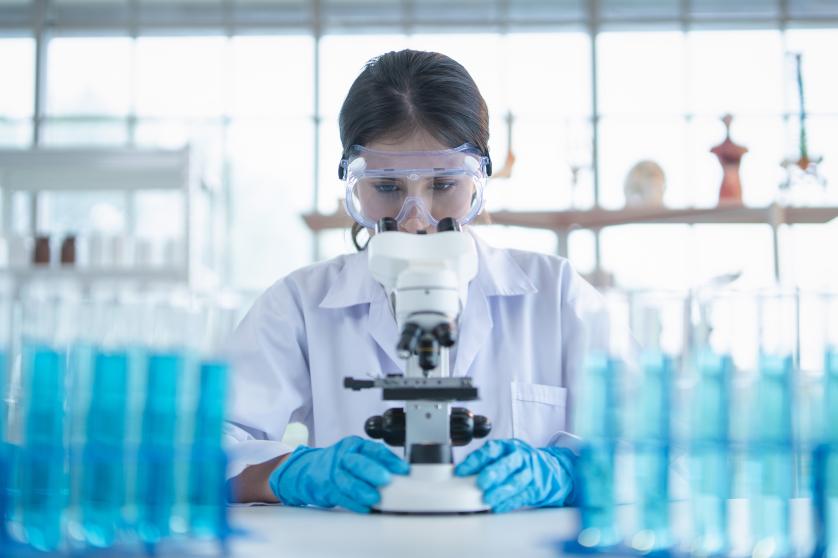 Técnico de laboratorio mirando por el microscopio mientras examina una muestra genómica durante una investigación en el laboratorio.