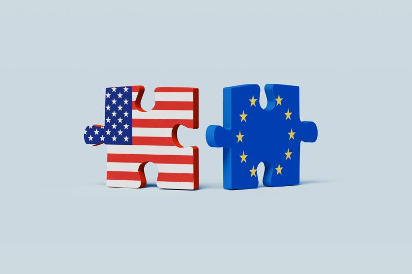 A symbolic composition featuring two puzzle pieces positioned closely together, one displaying the colors of the U.S. flag and the other featuring the European Union (EU) flag.