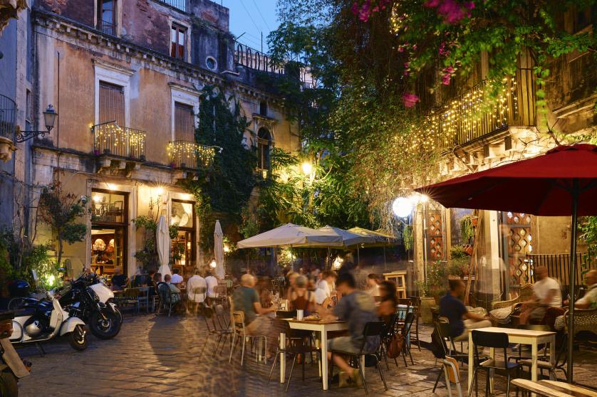 People dining outside restaurants and bars at dusk in Catania
