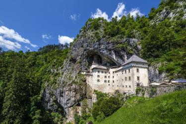 Predjama Castle built into a limestone cave entrance with a green hillside and blue sky, Slovenia