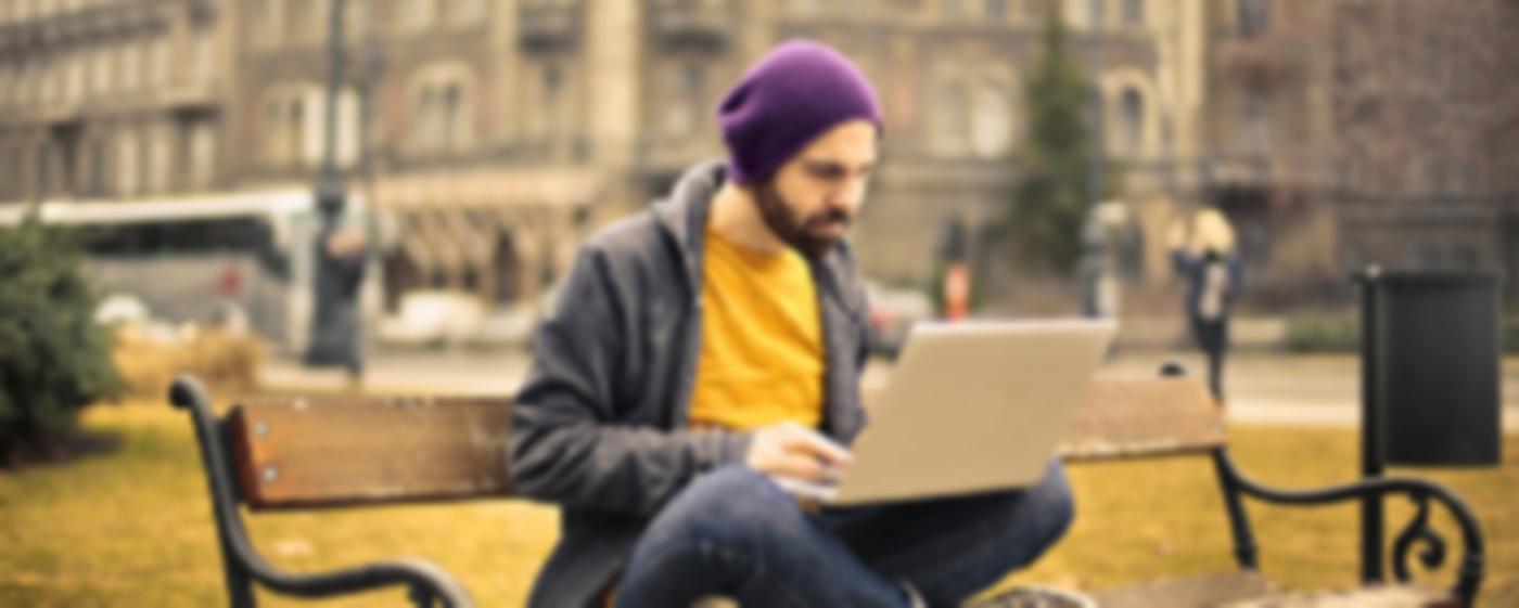 A young man sitting on a bench and working on a laptop