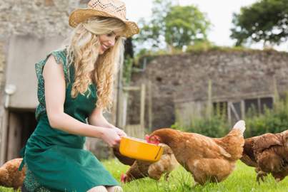 Νεαρή γυναίκα ταίζει κοτόπουλα