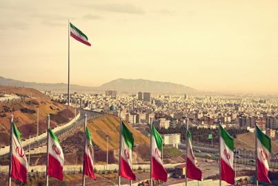 Řada íránských vlajek před panoramatem Teheránu