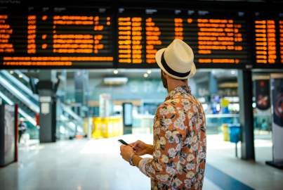 A man in a hat looks at a departures board in a station