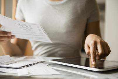A woman compares information on paper bank statements to what is on a tablet screen