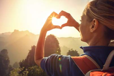 Young woman hiking in the mountains, makes a heart shape finger frame