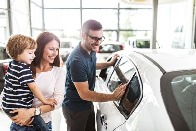 Young happy family enjoying while buying a new car in a showroom.