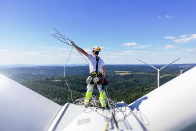 Professional rope access technician standing on roof (hub) of wind turbine and pulling rope up