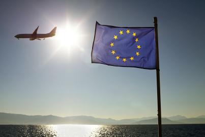 European Union Flag Against Sun & Sea With Plane