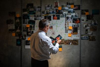 A man in front of a board with evidence solving crime