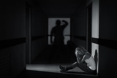 Mujer joven sentada en un pasillo vacío cubriéndose los ojos bajo la sombra de un hombre