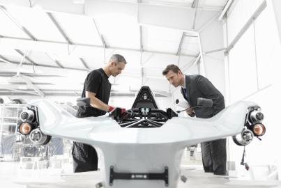 Engineer and automotive designer inspecting part-built supercar in car factory