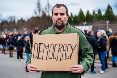 Man protester holding placard with text "Democracy" on the city street.