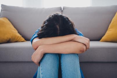 Female sitting with her head down, expressing emotions of sadness and stress, in a cozy and stylish indoor living space