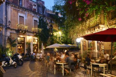 People dining outside restaurants and bars at dusk in Catania