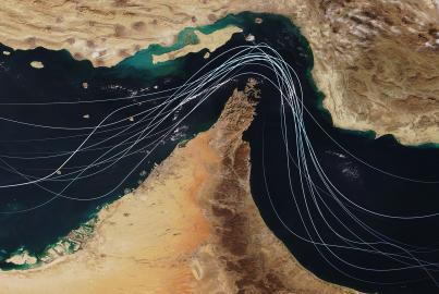 Satellite view of the Strait of Hormuz with white graphic lines representing global shipping lanes and maritime traffic between the Persian Gulf and Gulf of Oman