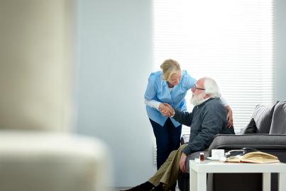 Female caregiver helping senior man get up from couch